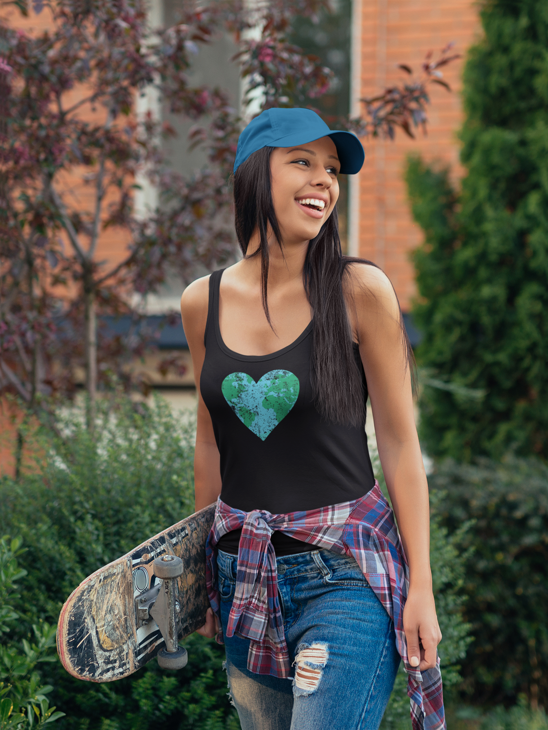 Woman holding a skateboard with a heart design on her tank top, standing outdoors.